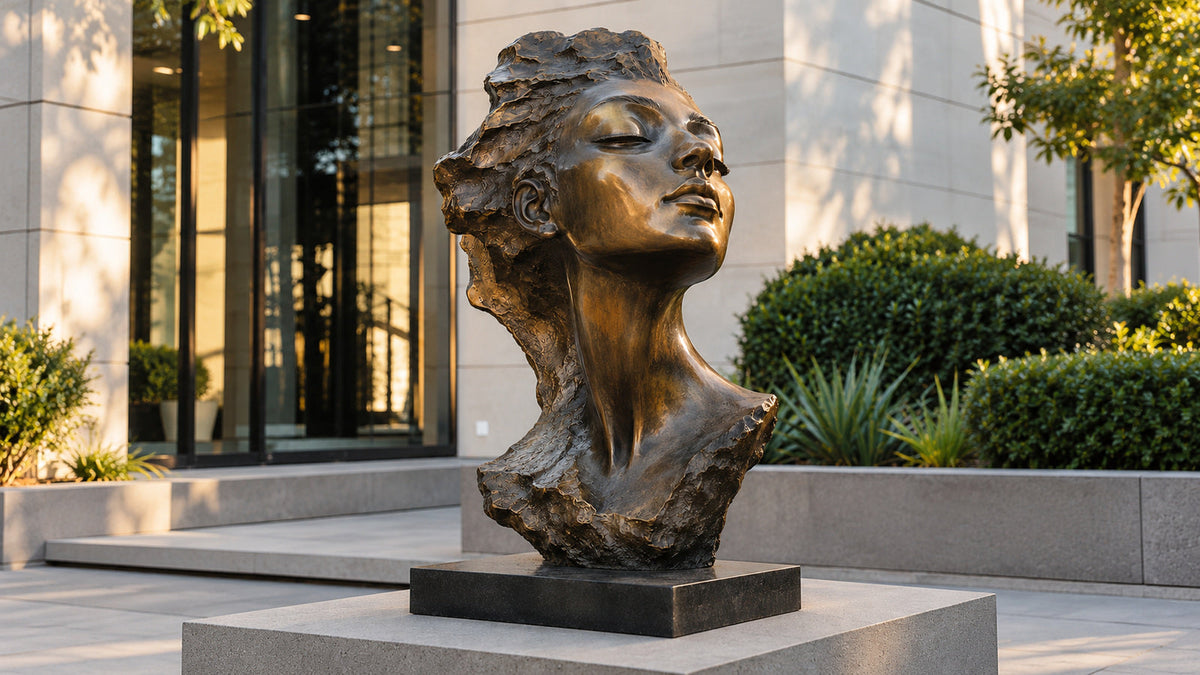 Bronze female portrait bust with textured hair on a pedestal outside a modern building.