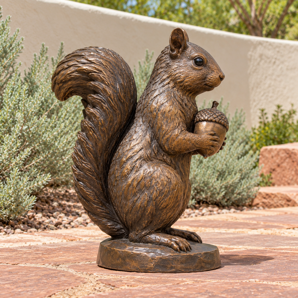Chestnut Keeper Warm Bronze Seated Squirrel with Acorn sculpture, 90 degree view in Utah residential courtyard with cream rendered curved wall, low sagebrush and reddish flagstone.