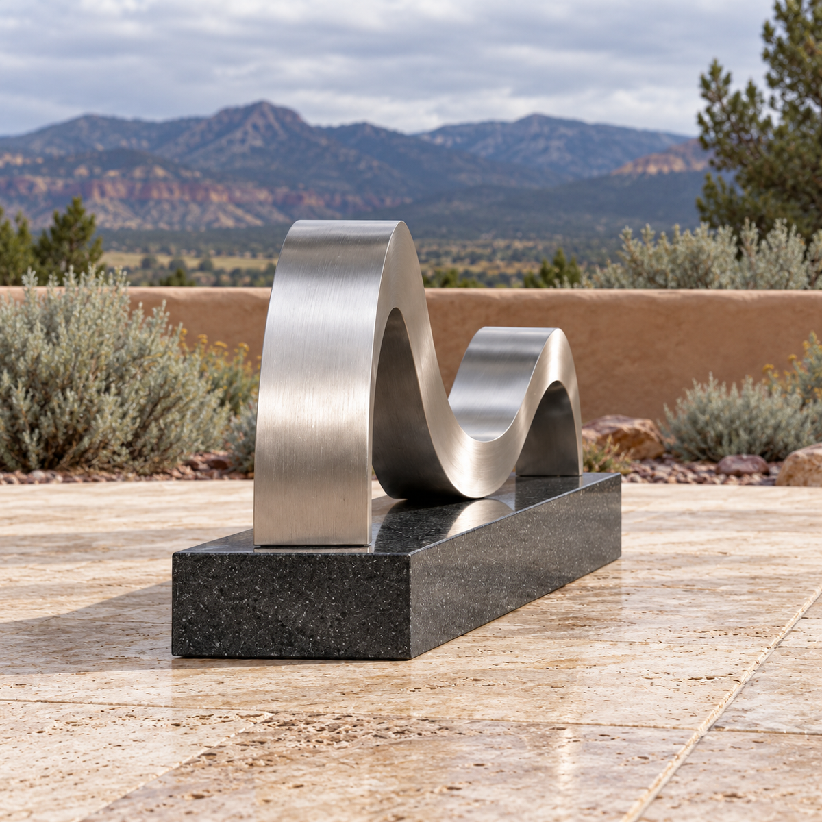 Side profile of Continuing Shore brushed stainless steel ribbon memorial sculpture in a different architectural or garden setting.