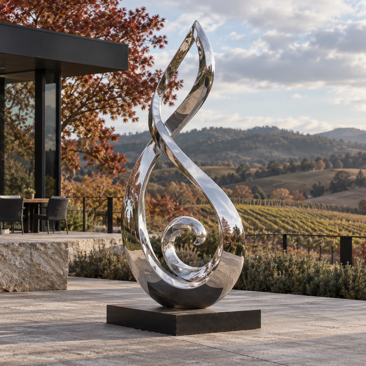 Flowing Spirit mirror stainless steel abstract sculpture on a stone terrace overlooking vineyard rows and autumn foliage.