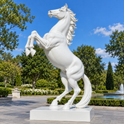 Noble Spirit white marble rearing horse sculpture displayed in a formal landscaped garden with fountain, trees, and blue sky.