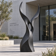 Twin Ascent dark bronze abstract rising sculpture displayed outdoors in front of a contemporary art center with modern architecture and landscaped surroundings.